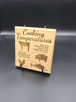 A square laser-engraved oak wood magnet showing a chart of internal meat temperatures for beef, pork, and poultry, resting on a stainless steel refrigerator door