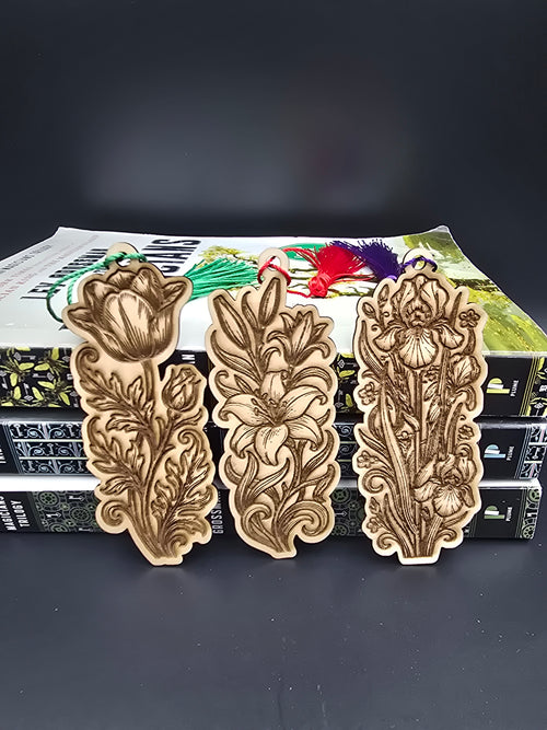 A collection of 4 laser engraved wooden bookmarks with colorful tassels that measure 4" x 1.5, slightly smaller than standard bookmark size. Each bookmark is engraved to look like a different flower, the first like a rose, the second like a lilly, the third to look like an iris. 