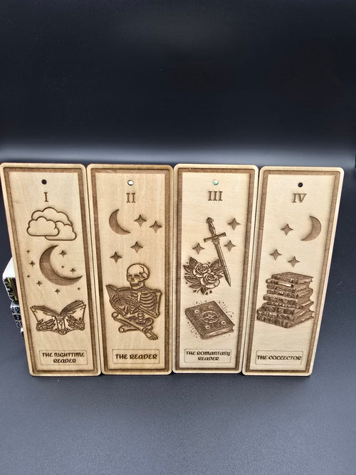 A collection of 4 laser engraved wooden bookmarks with colorful tassels that measure 6" x 2", standard bookmark size. Designed to look like wooden bookmark tarot cards, the first one is "The Nighttime Reader" the second one is "The Reader" The third one is "The Romantasy Reader" and the fourth one is "The Collector" 