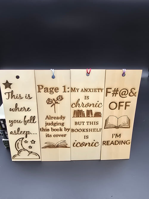 A collection of 4 laser engraved wooden bookmarks with colorful tassels that measure 6" x 2", standard bookmark size. Features laser engraved phrases that read "this is where you fell asleep" "page 1 already judging this book by its cover" "my anxiety is chronic but this bookshelf is iconic" and "fuck off i'm reading"