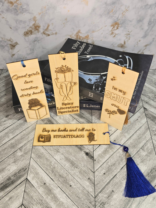 A collection of 4 laser engraved wooden bookmarks with colorful tassels that measure 6" x 2", standard bookmark size. Adult themed laser engraved phrases that read "good girls love reading dirty books" "spicy literature specialist" in my smut era" and "buy me books and tell me to stfuattdlagg"