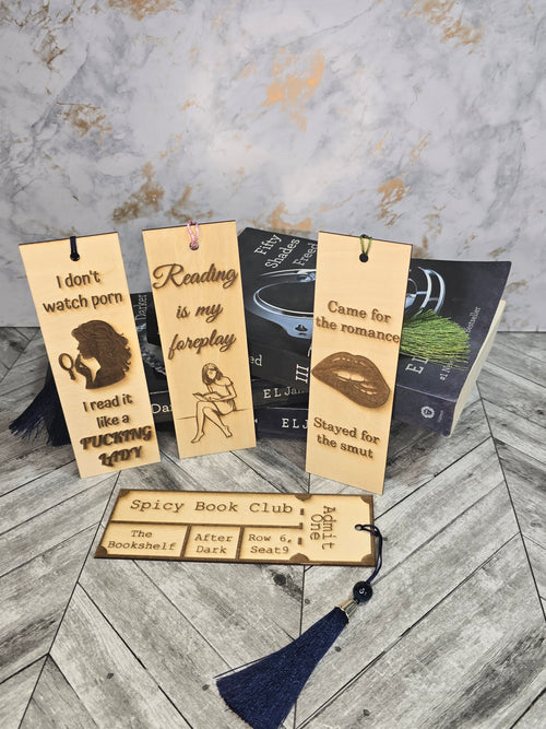 A collection of 4 laser engraved wooden bookmarks with colorful tassels that measure 6" x 2", standard bookmark size. Adult themed laser engraved phrases that read "i don't watch porn i read it like a fucking lady" "reading is my foreplay" "came for the romance stayed for the smut" "spicy book club" 