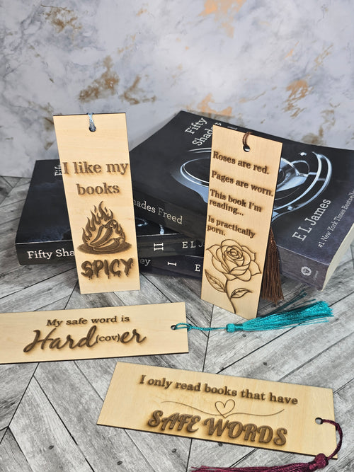 A collection of 4 laser engraved wooden bookmarks with colorful tassels that measure 6" x 2", standard bookmark size. Adult themed laser engraved phrases that read "I like my books spicy" "roses are red pages are worn this book i'm reading is practically porn" "my safe word is hardcover" "i only read books that have safe words" 