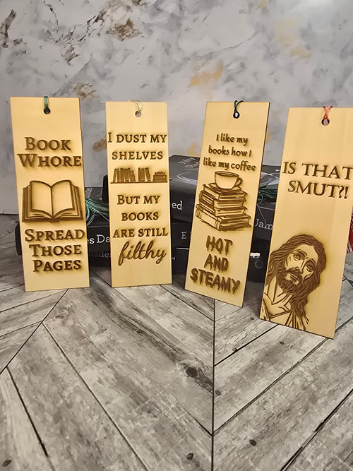 A collection of 4 laser engraved wooden bookmarks with colorful tassels that measure 6" x 2", standard bookmark size. Adult themed laser engraved quotes that read "book whore spread those pages" "i dust my shelves but my books are still filthy" "i like my books how I like my coffee hot and steamy" and a picture of Jesus saying "is that smut"