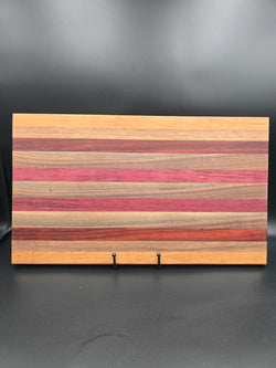 A handcrafted rectangular wooden serving board featuring a horizontal striped pattern of purpleheart, padauk, walnut, and cherry hardwoods, showcasing vibrant natural colors and a polished finish.