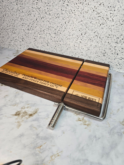 modern handcrafted wooden cheese board made from walnut, maple, rosewood, red heart and yellow heart, built in silver cheese slicer, perfect for charcuterie, cheese, and appetizers. Laser engraved with the phrase "charcuterie french word for cheese and other fancy shit"