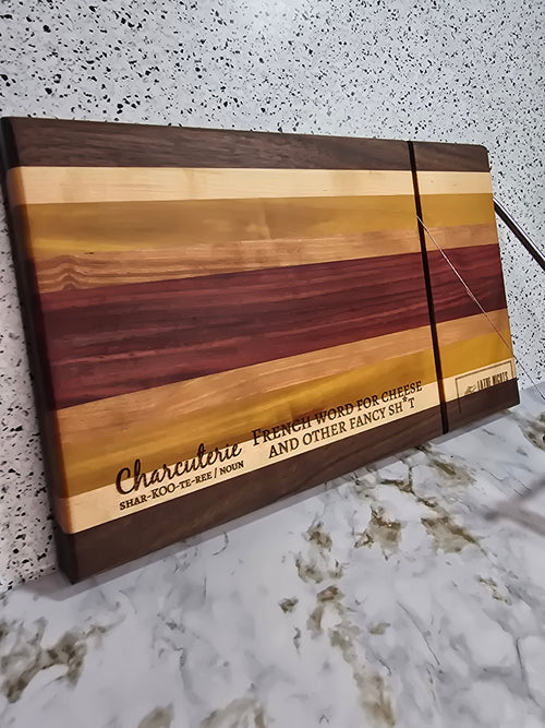 modern handcrafted wooden cheese board made from walnut, maple, rosewood, red heart and yellow heart, built in silver cheese slicer, perfect for charcuterie, cheese, and appetizers. Laser engraved with the phrase "charcuterie french word for cheese and other fancy shit"