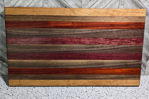 A handcrafted rectangular wooden serving board featuring a horizontal striped pattern of purpleheart, padauk, walnut, and cherry hardwoods, showcasing vibrant natural colors and a polished finish.