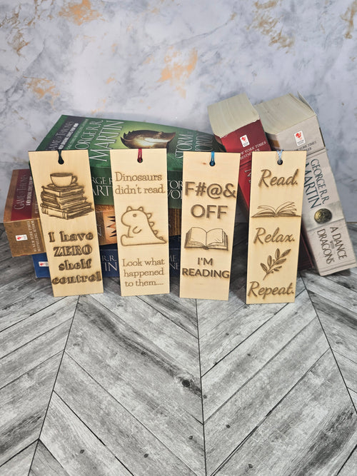 A collection of 4 laser engraved wooden bookmarks with colorful tassels that measure 6" x 2", standard bookmark size. Features laser engraved quotes like 'i have zero shelf control' and 'dinosaurs didn't read. look what happened to them' and F#@& off I'm reading' and 'read. relax. repeat.'