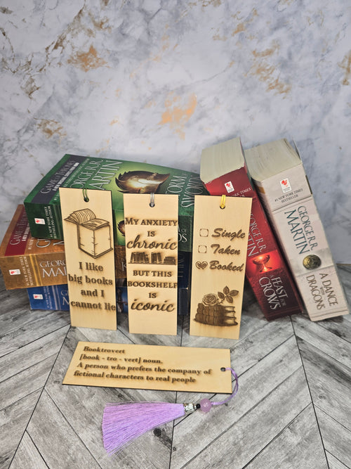 A collection of 4 laser engraved wooden bookmarks with colorful tassels that measure 6" x 2", standard bookmark size. Features laser engraved sayings like "I like big books and i cannot lie" "my anxiety is chronic but this bookshelf is iconic" "single taken booked" and "booktrovert"
