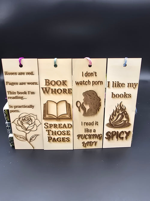 A collection of 4 laser engraved wooden bookmarks with colorful tassels that measure 6" x 2", standard bookmark size. Adult themed laser engraved phrases that read "roses are red pages are worn this book i'm reading is practically porn" "book whore spread those pages" "i don't watch porn i read it like a fucking lady" "i like my books spicy"