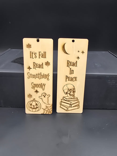 Two laser engraved, halloween themed wooden bookmarks. The first reads, "It's fall, read something spooky" and the second reads, "read in peace" 