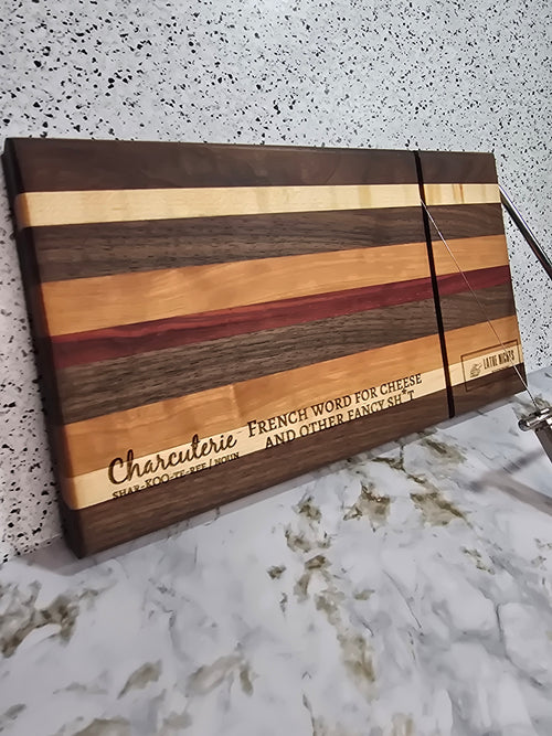 modern handcrafted wooden cheese board made from walnut, maple, cherry and padauk, built in silver cheese slicer, perfect for charcuterie, cheese, and appetizers. Laser engraved with the phrase "charcuterie french word for cheese and other fancy shit"